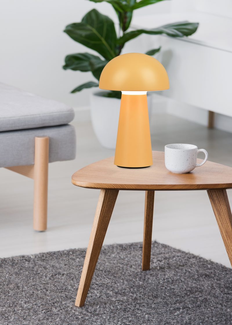 Cup on a wooden coffee table and blurry foreground with graphic pillows on a gray sofa in a white living room interior