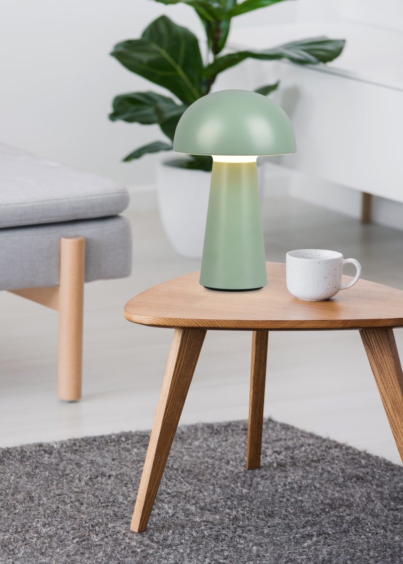 Cup on a wooden coffee table and blurry foreground with graphic pillows on a gray sofa in a white living room interior