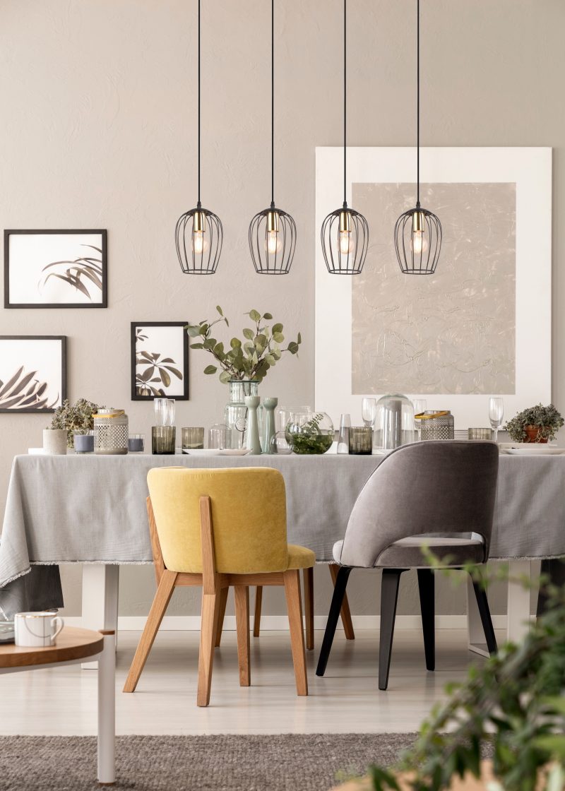 Grey and yellow chair at table under lamp in dining room interior with posters and plants. Real photo