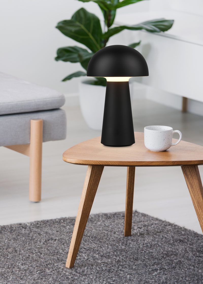 Cup on a wooden coffee table and blurry foreground with graphic pillows on a gray sofa in a white living room interior